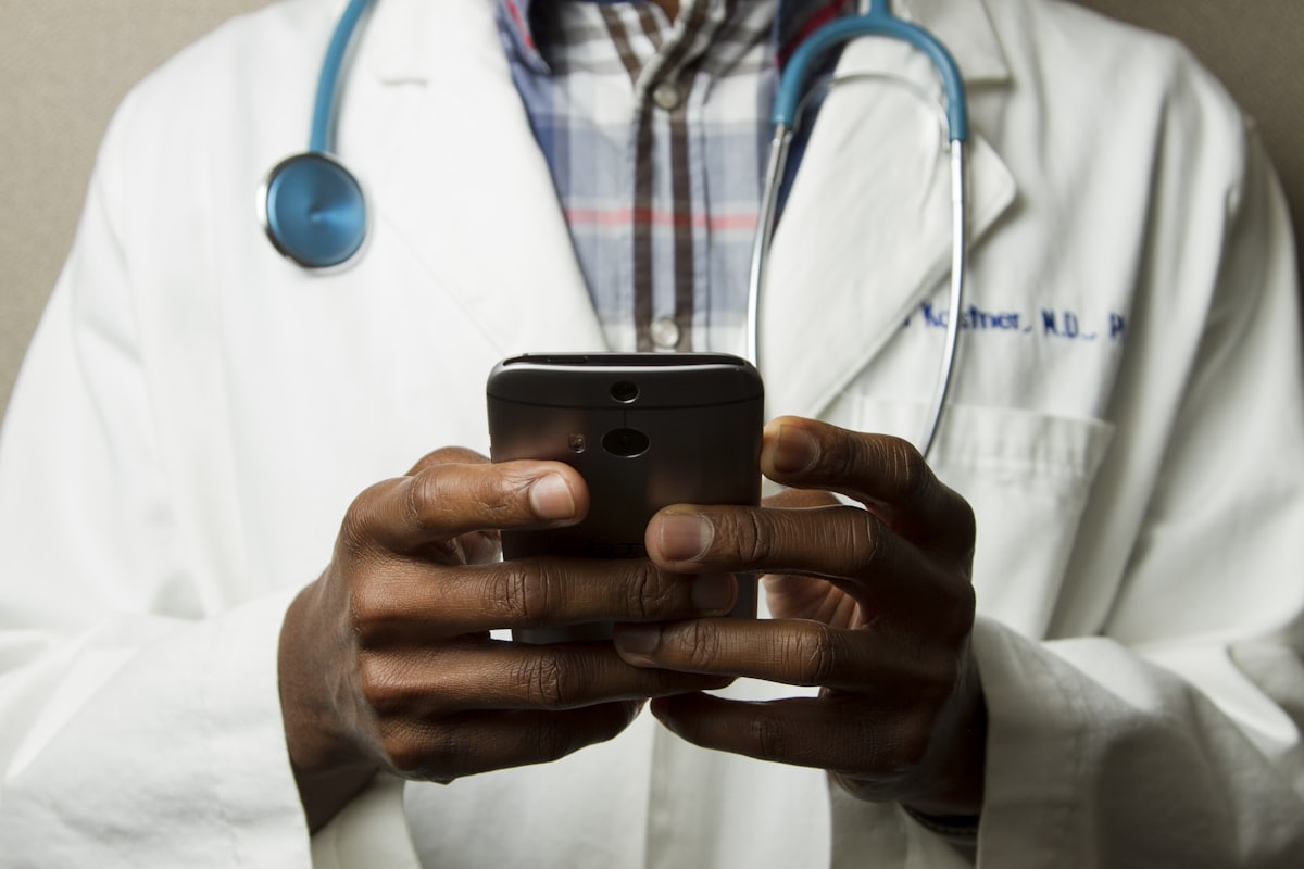 Profissional de saúde de jaleco e estetoscópio usando o celular